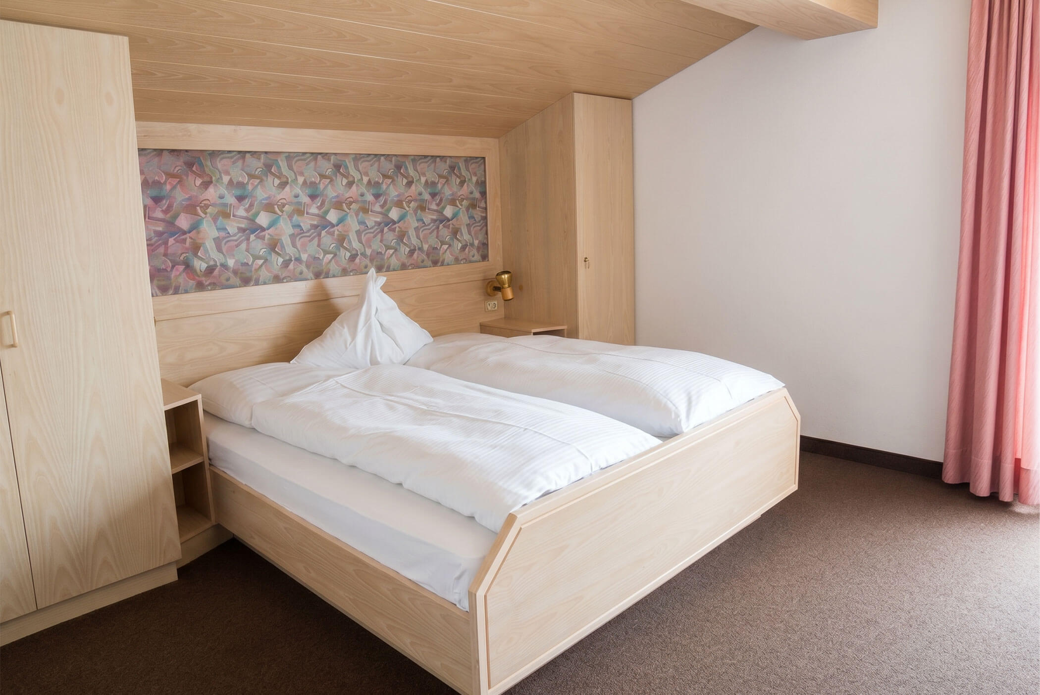 Minimalistisches Hotelzimmer mit einem Doppelbett, hellen Holzmöbeln, weißer Bettwäsche und rosa Vorhängen. - Hotel Mooserhof