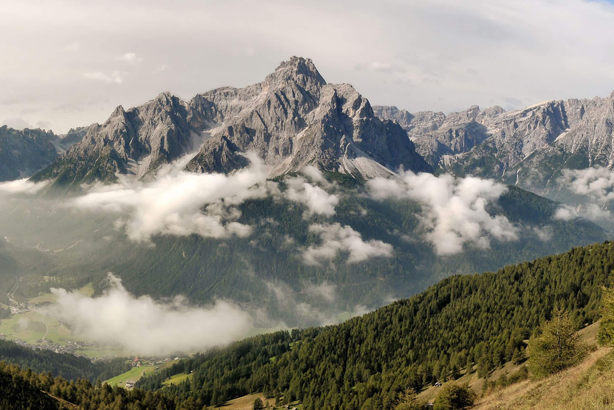 Zackige Berggipfel erheben sich über einem grünen, bewaldeten Tal, und Wolken ziehen über die Landschaft. - Hotel Mooserhof