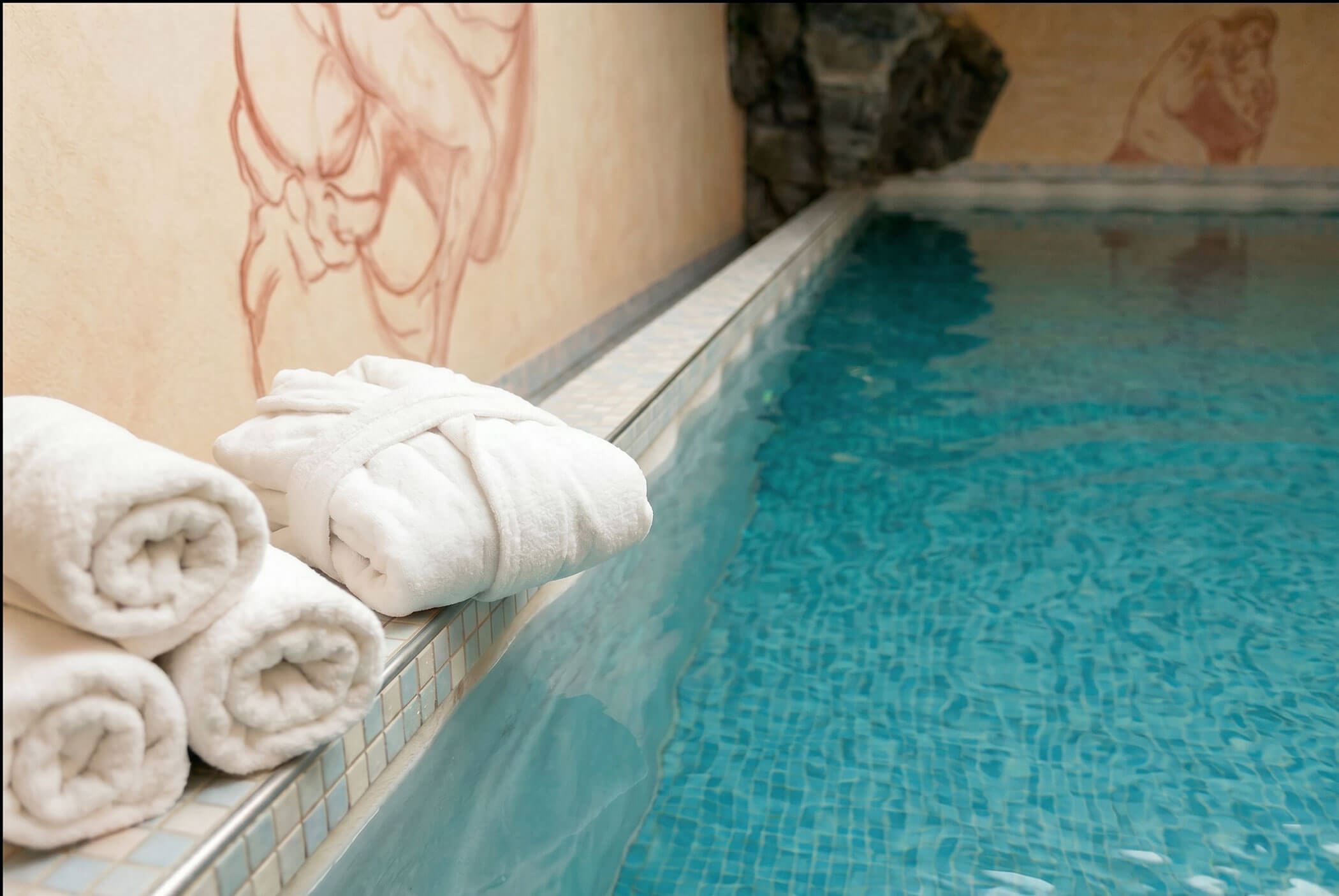 Weiße Handtücher und ein Bademantel liegen fein säuberlich am Rand des Hallenbades mit blauem Wasser. - Hotel Mooserhof
