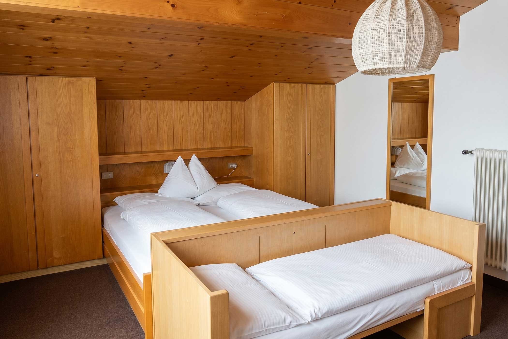 Ein gemütliches Schlafzimmer aus Holz mit einem Doppelbett, einem Einzelbett, einem Kleiderschrank und einer Deckenlampe aus Korbgeflecht. - Hotel Mooserhof