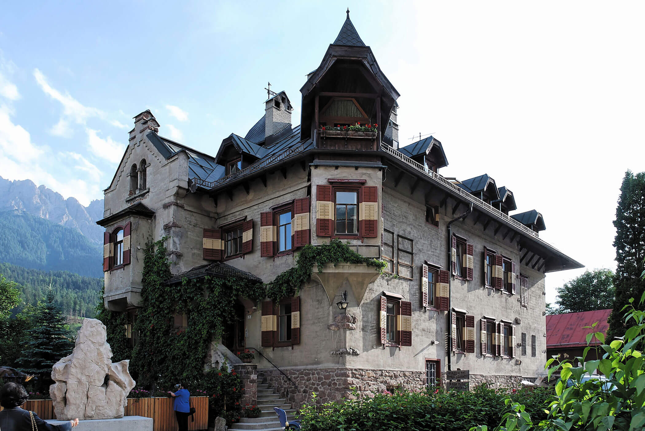 Großes, altes Haus mit Steinmauern, roten Fensterläden und Balkonen, umgeben von viel Grün und Bergen. - Hotel Mooserhof