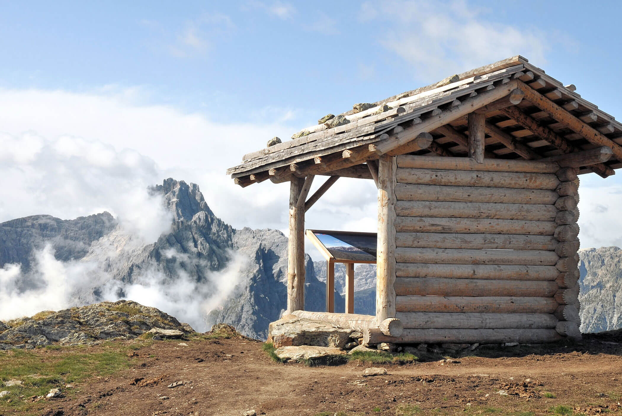 Eine kleine Holzhütte liegt an einem Berghang mit felsigen Gipfeln und Wolken im Hintergrund. - Hotel Mooserhof